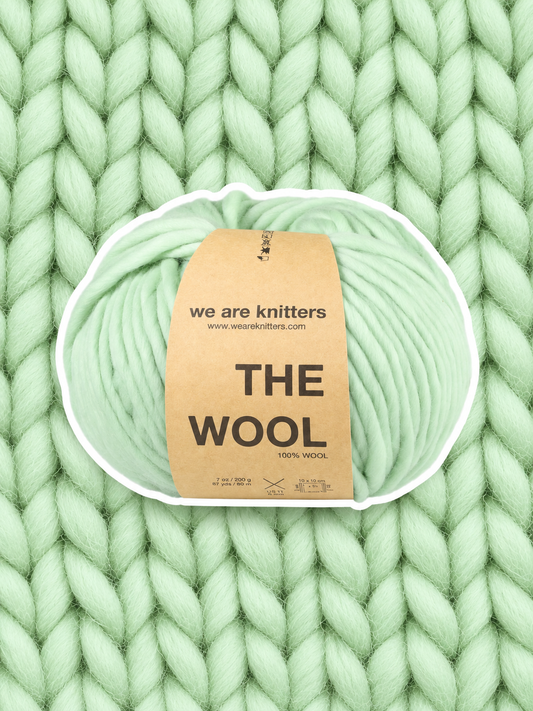 The Wool Sage Green yarn ball on a matching knit swatch